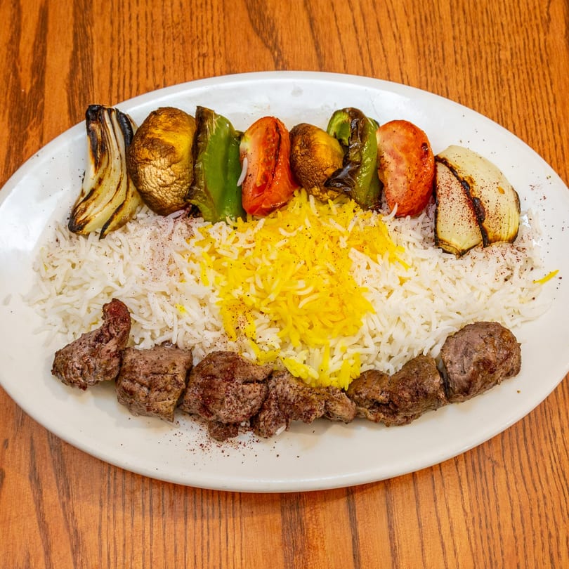 Persian beef kabob with grilled vegetables, white rice, and saffron rice on a white plate.