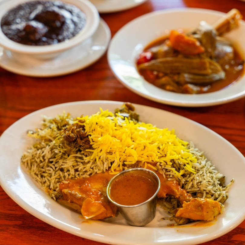 Plates of Persian stews and rice dishes, including a chicken and rice dish with yellow saffron rice.