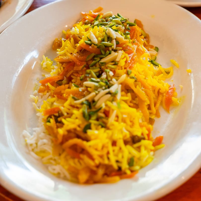 Persian rice dish with saffron, orange peel, pistachios, and almonds on a white plate.