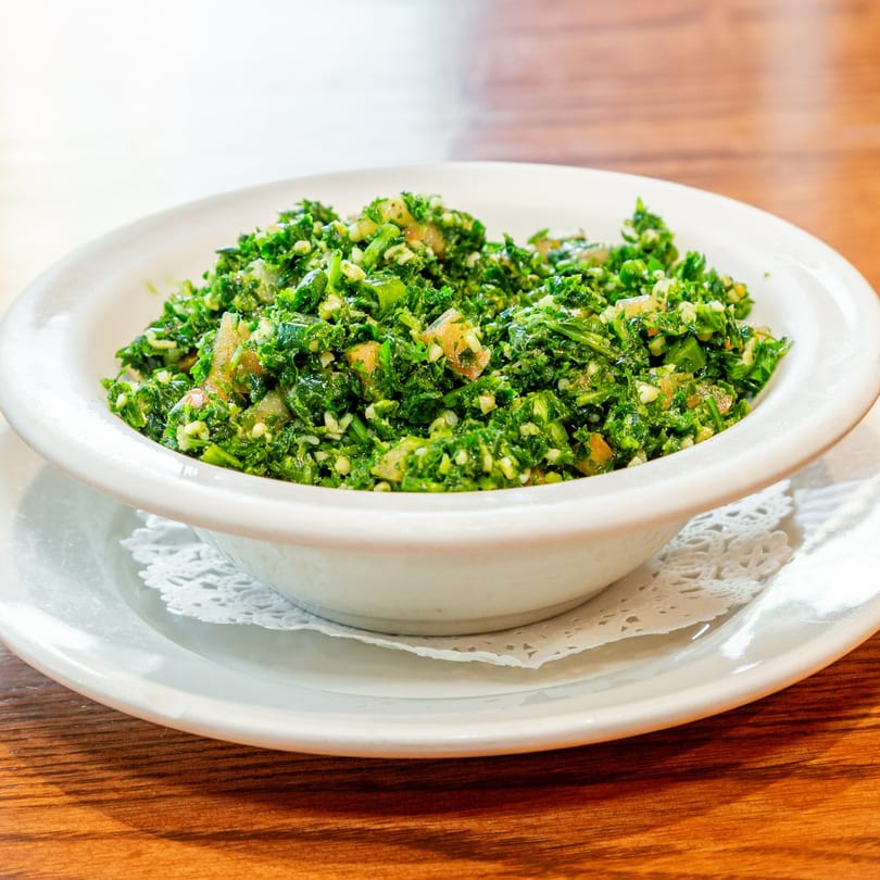 A white bowl filled with vibrant green Tabbouleh salad, featuring parsley, tomatoes, and bulgur.