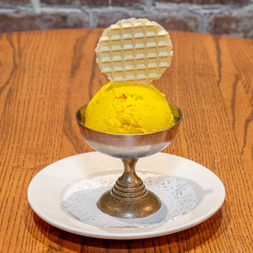 Saffron ice cream in a silver goblet with a waffle crisp, on a white plate with doily.