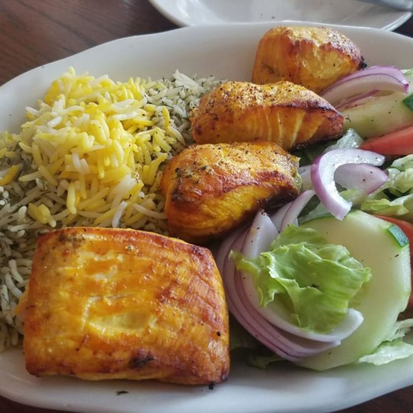 Persian dish with four pieces of grilled salmon, yellow rice, and a side salad.