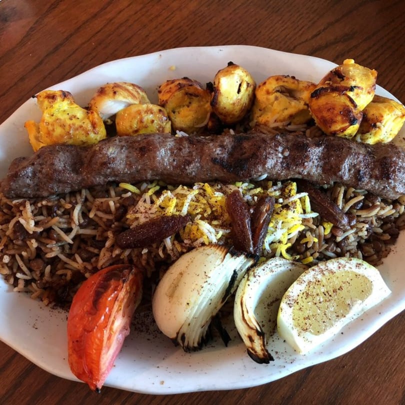 A Persian dish with a long ground meat kabob, chicken pieces, rice, grilled tomato, and onions.