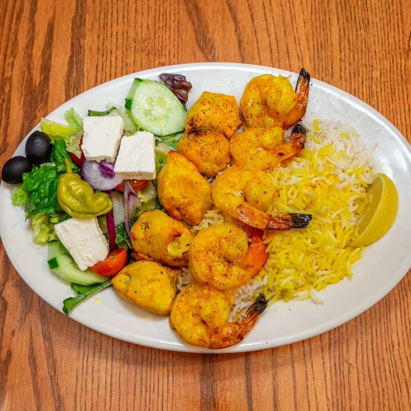 Persian shrimp and chicken kabobs with saffron rice, Greek salad, and a lemon wedge.