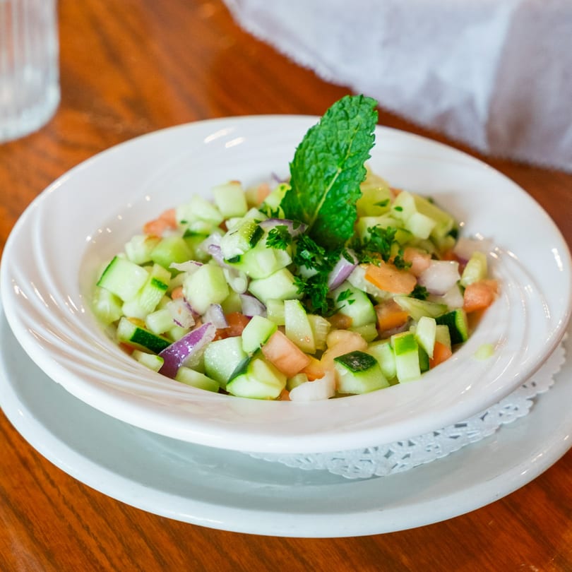 A white bowl of Shirazi salad with diced cucumbers, tomatoes, red onions, and mint.