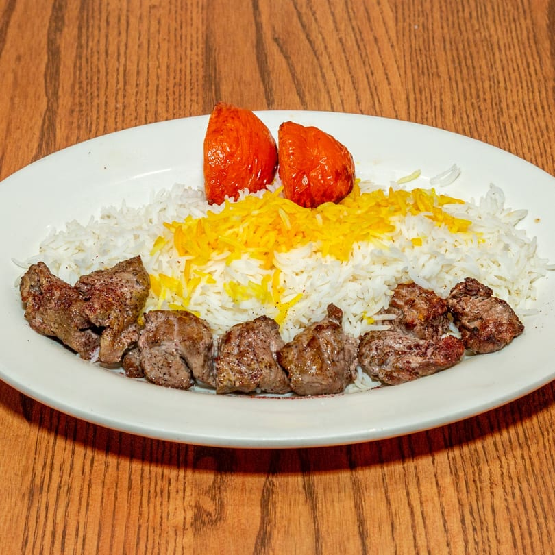 Persian dish with grilled meat, white rice, yellow saffron rice, and two roasted tomatoes.