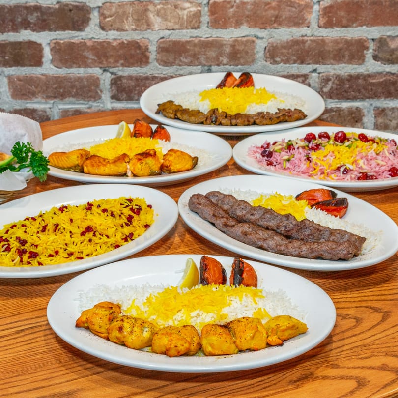 A table laden with various Persian kabob dishes, including chicken, koobideh, and salmon, with rice.