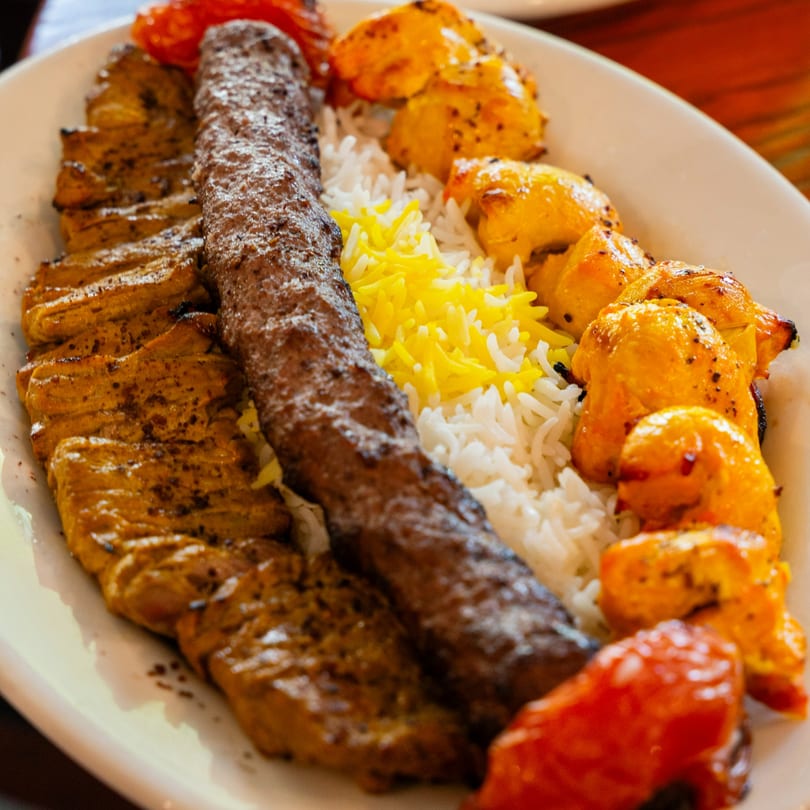 A Persian kabob platter with three types of grilled meat, white rice, and saffron rice.